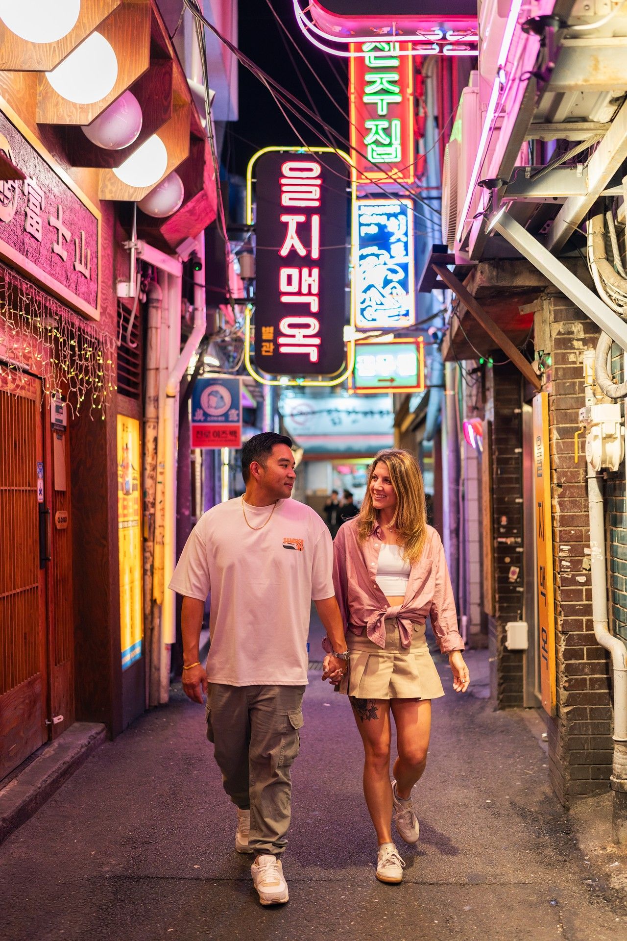 A couple walks together through a colorful neon-lit alley in Korea's nightlife district.