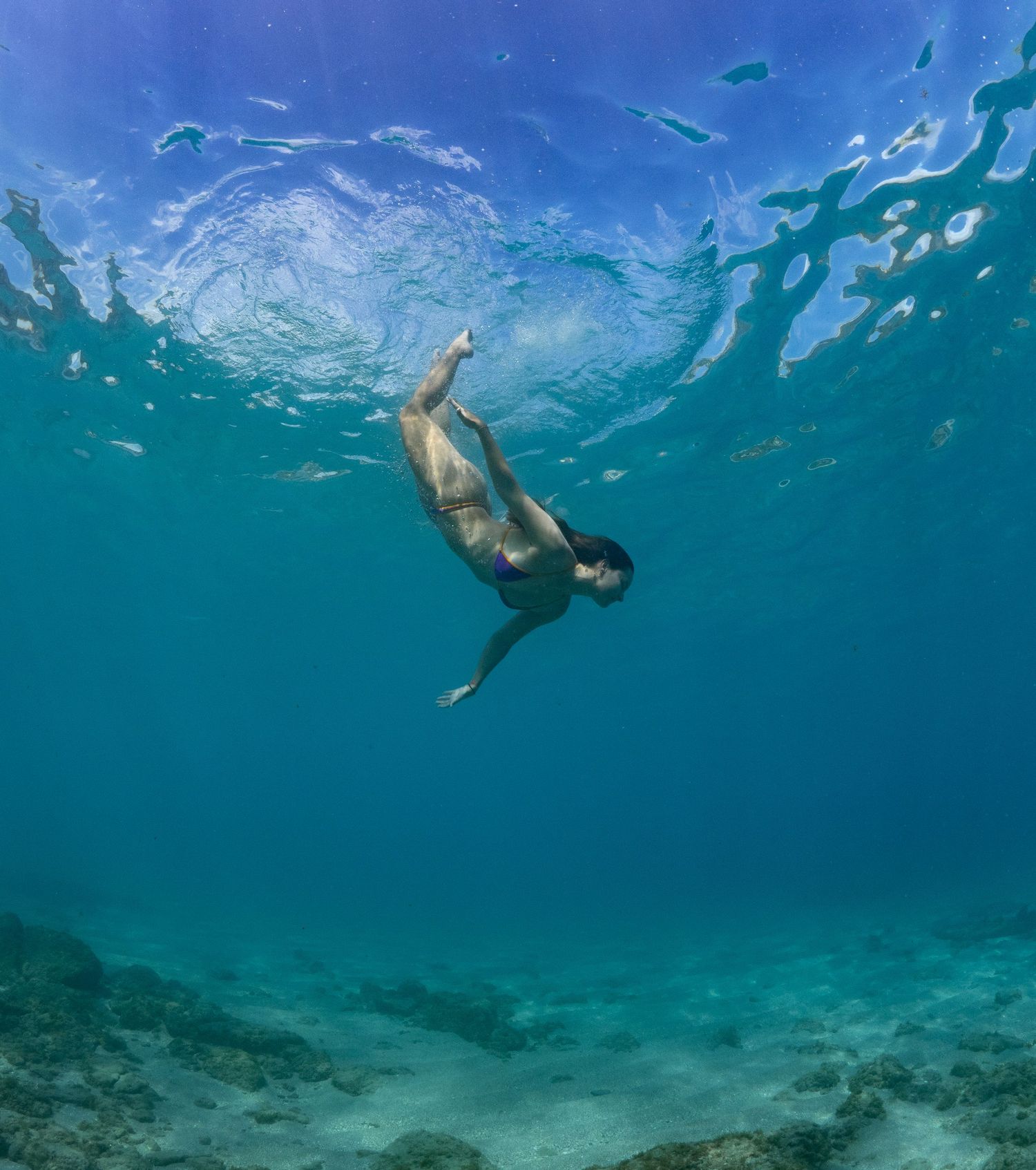 Snorkeler swimming in clear turquoise waters above sandy ocean floor with fish visible below.