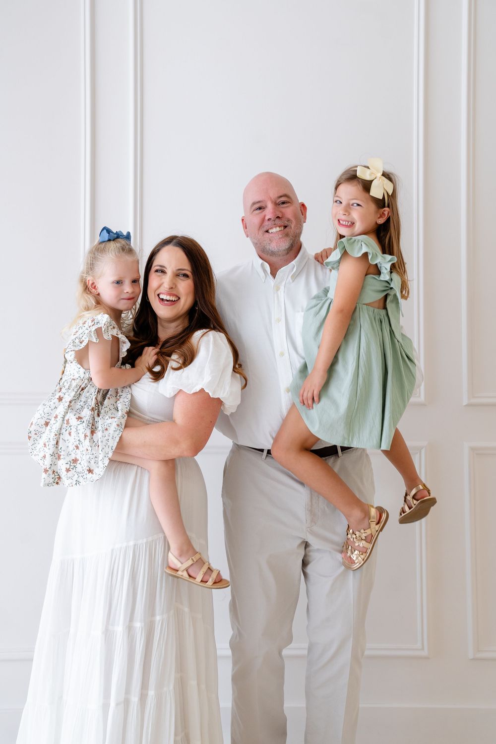 A family wearing coordinated white and mint green outfits poses playfully against a white paneled wall.