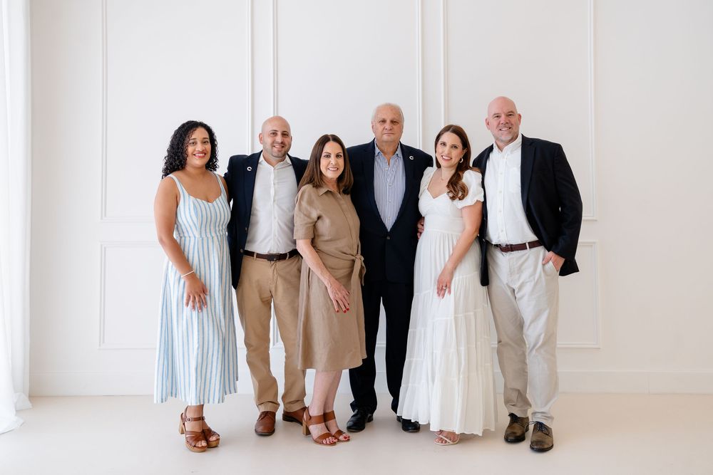A group of people dressed in light colored clothing sit together on a white floor against a bright white wall.