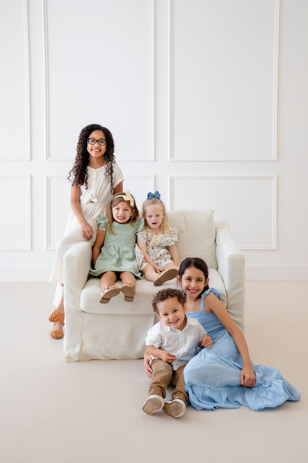 A family lounges together on a white couch in coordinated blue and white outfits for a casual photoshoot.
