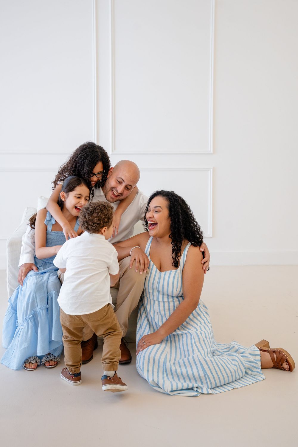 Family members share joyful moments together on a white floor in coordinated casual outfits.