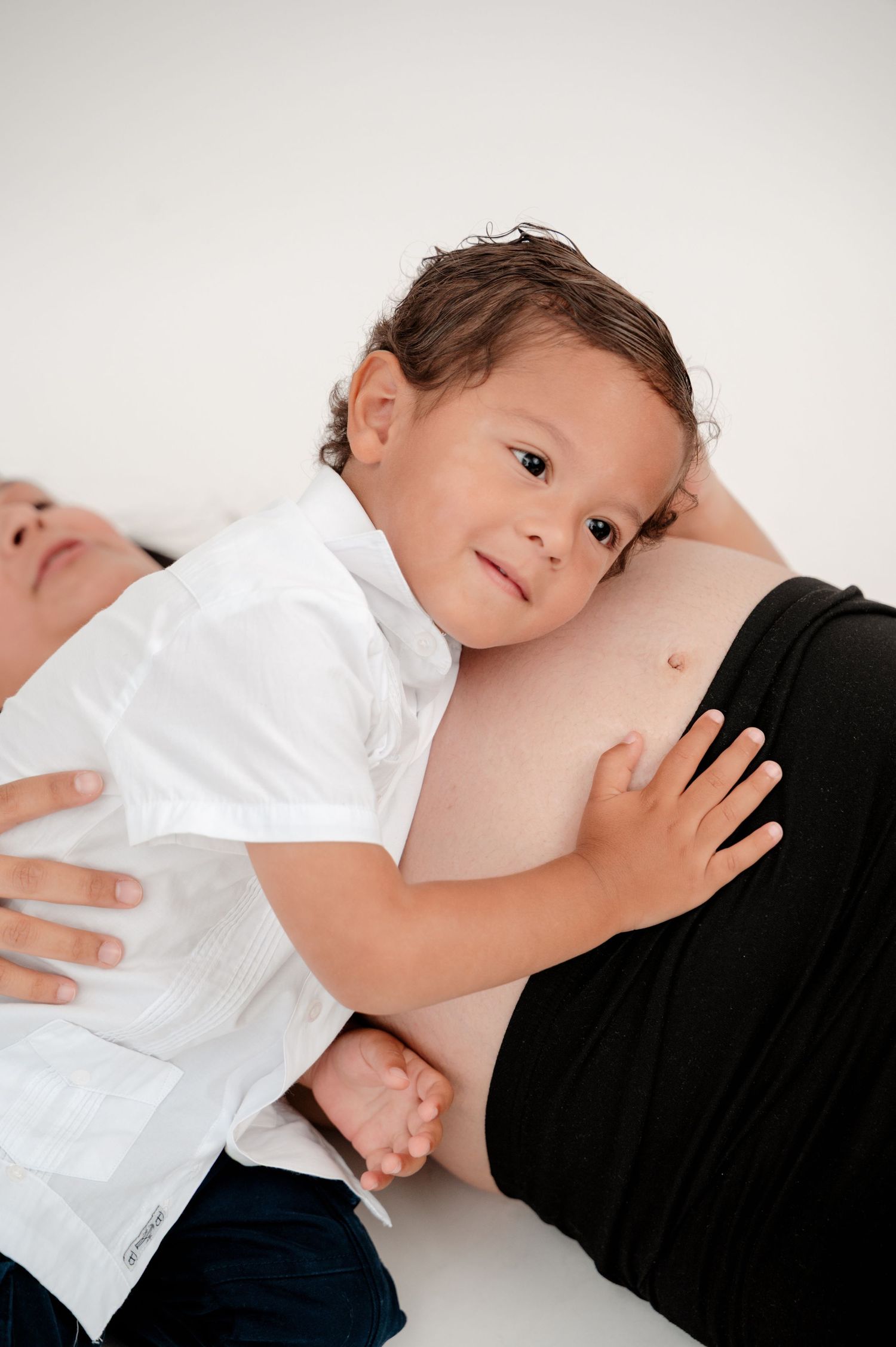 A child in a white shirt and dark pants lies on a white background in a series of artistic poses.
