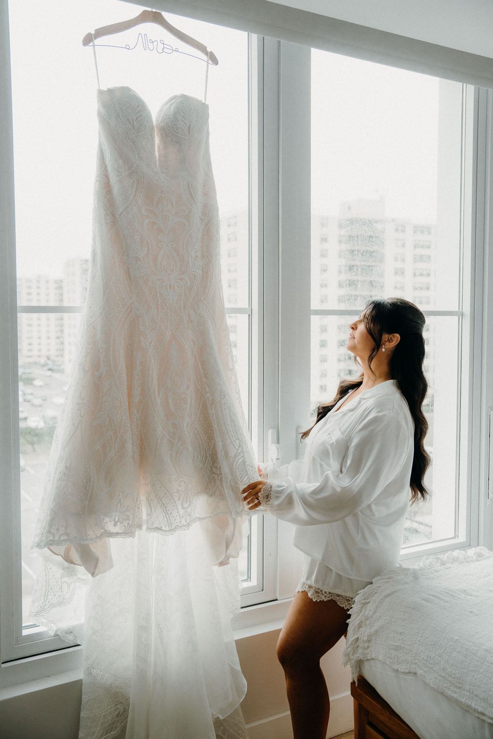 A sequence of photos showing a white wedding dress hanging in a bright window while someone adjusts and admires it.
