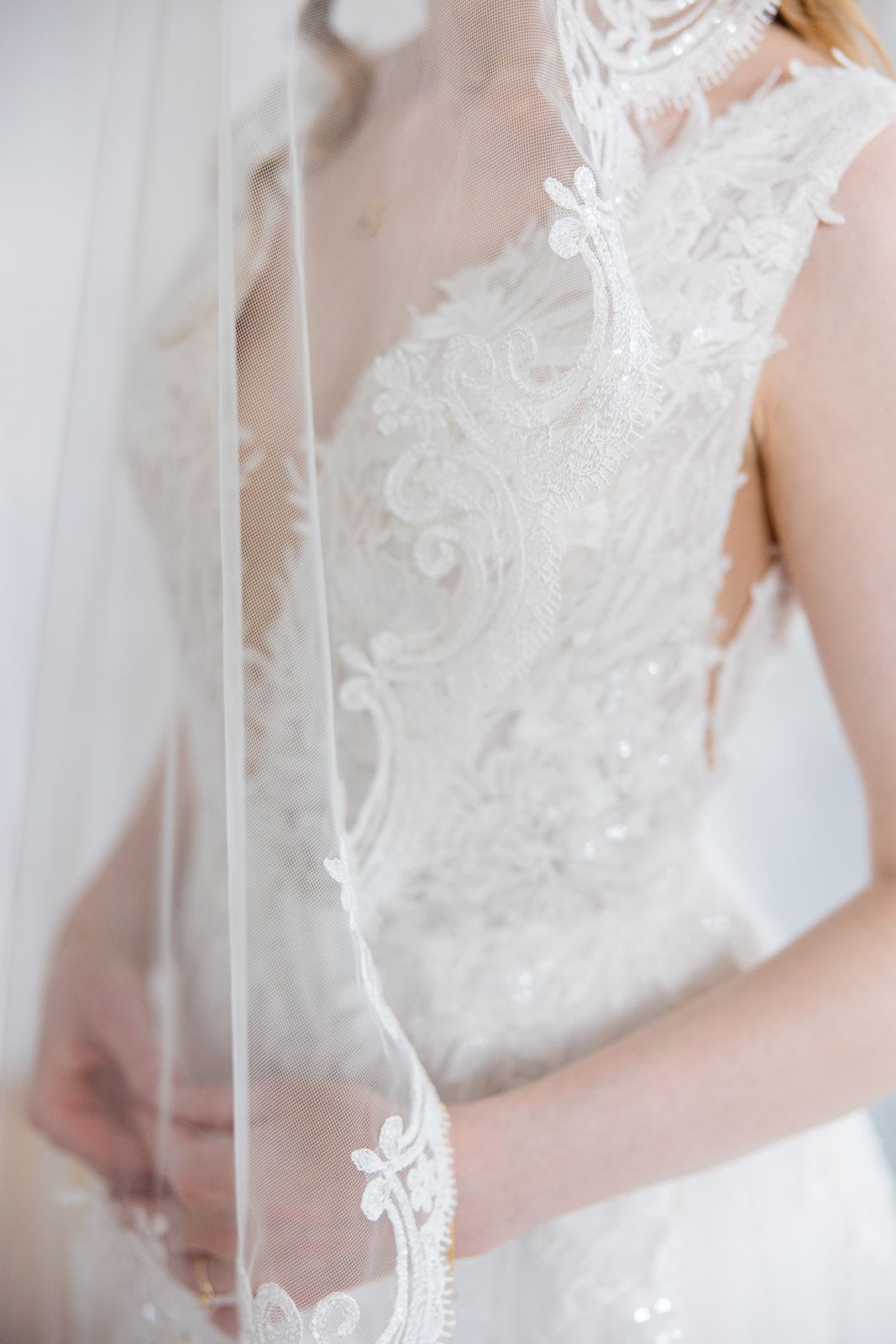 Close-up detail of delicate white lace and embroidery on a wedding dress with sheer veil.