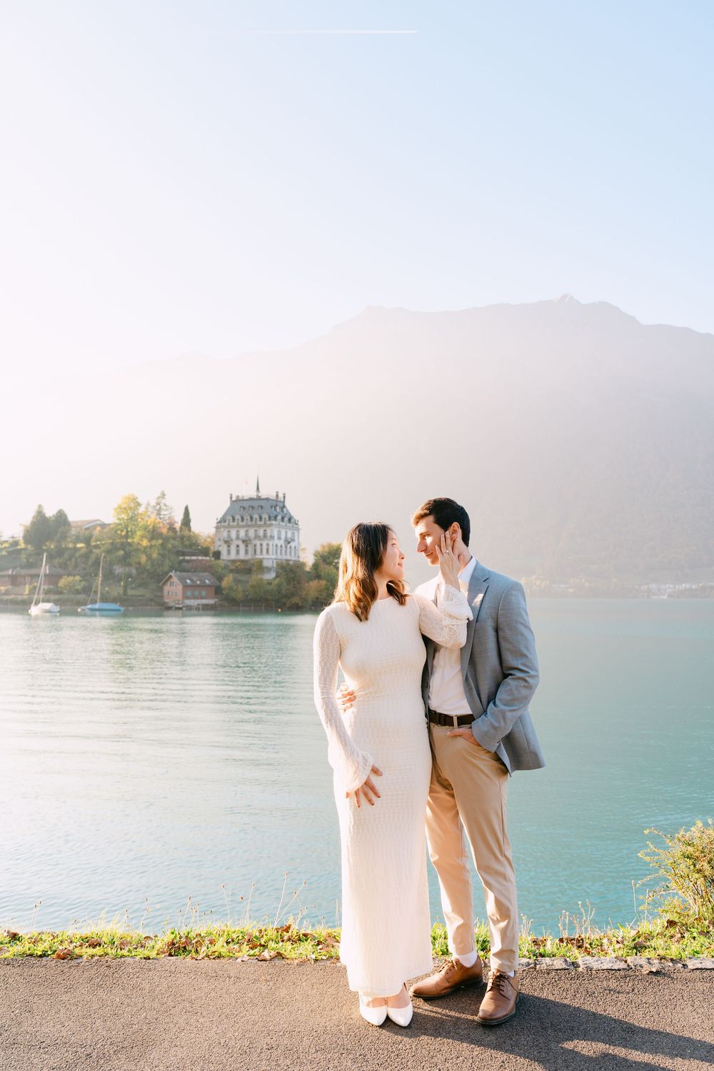 Couple enjoying a romantic moment by a scenic mountain lake with a historic castle visible in the background.