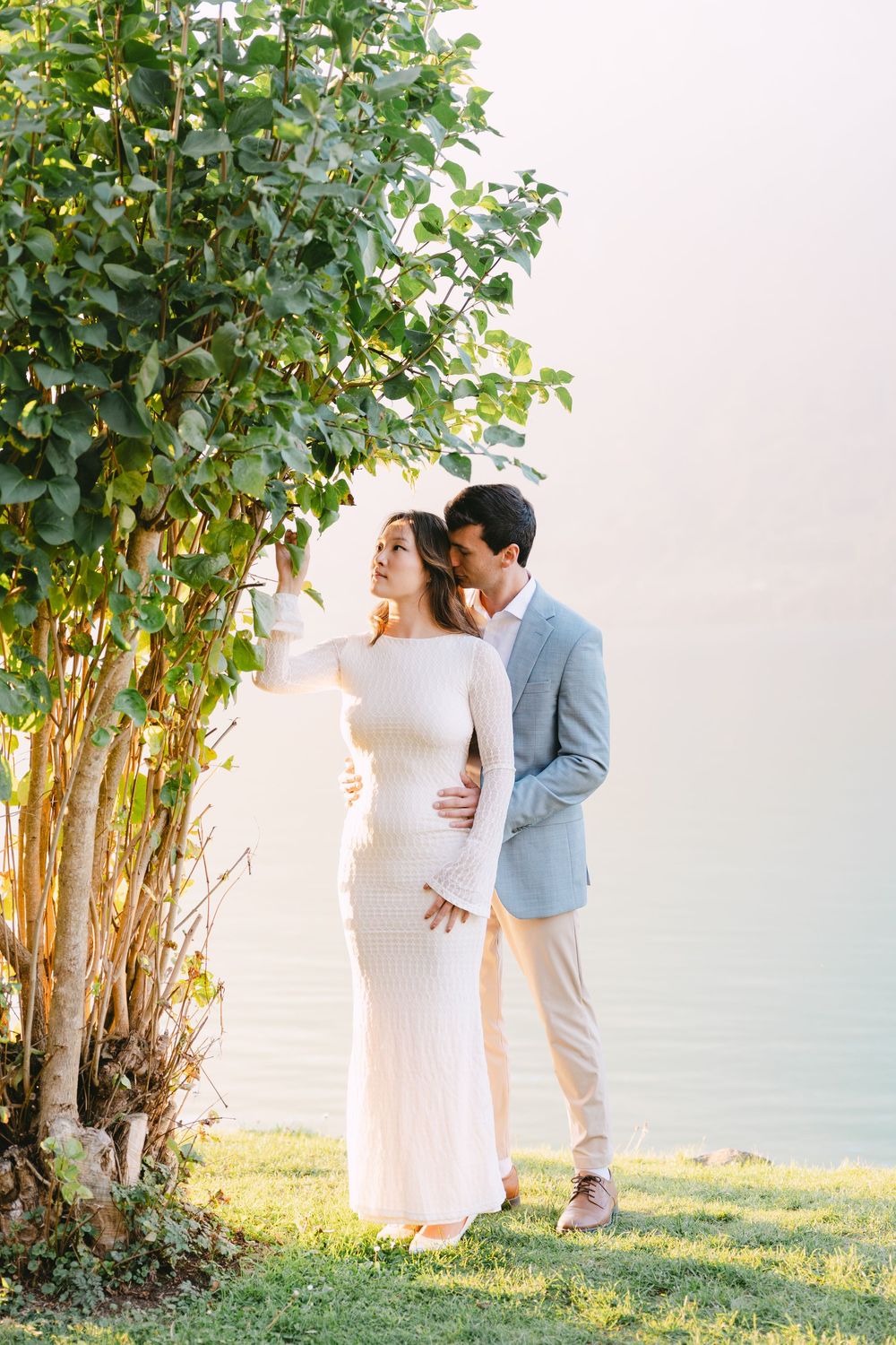 A couple shares an intimate moment at sunset surrounded by lush green trees in a garden setting.