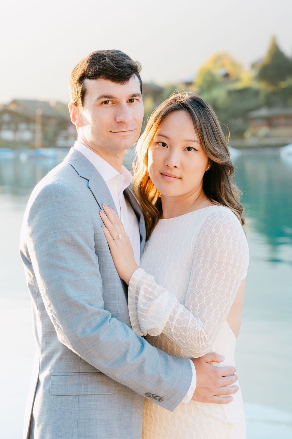 A romantic engagement photo session with a couple embracing by a serene waterfront in soft natural lighting at Lake Brienz in Switzerland.