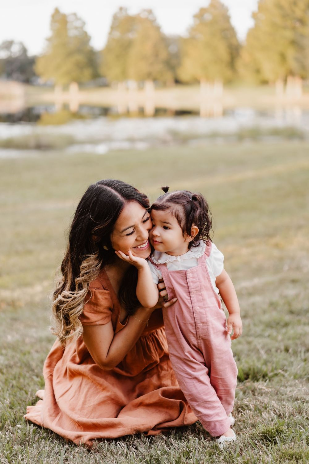 A tender moment captured in a grassy field during golden hour with matching peach and pink outfits.