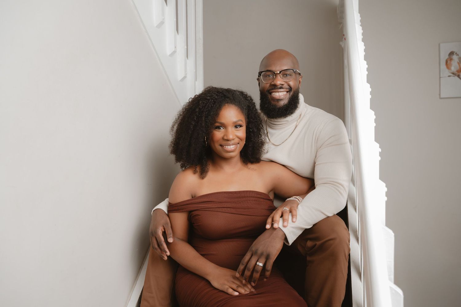 A couple poses together in coordinated brown and white outfits during an indoor photoshoot.