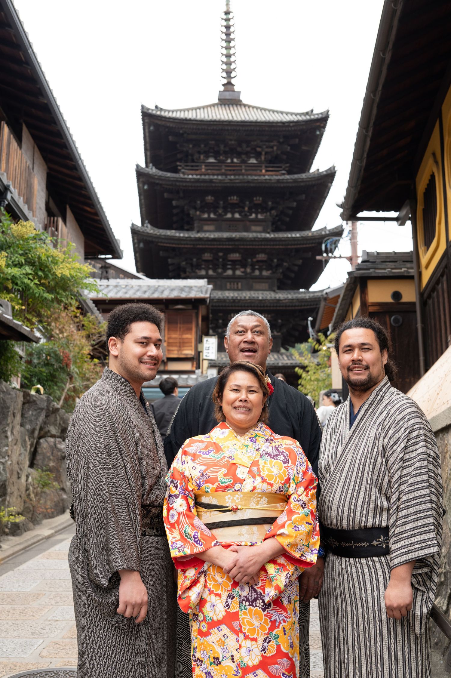 Family of four smiling in traditional Japanese attire before a historic pagoda.