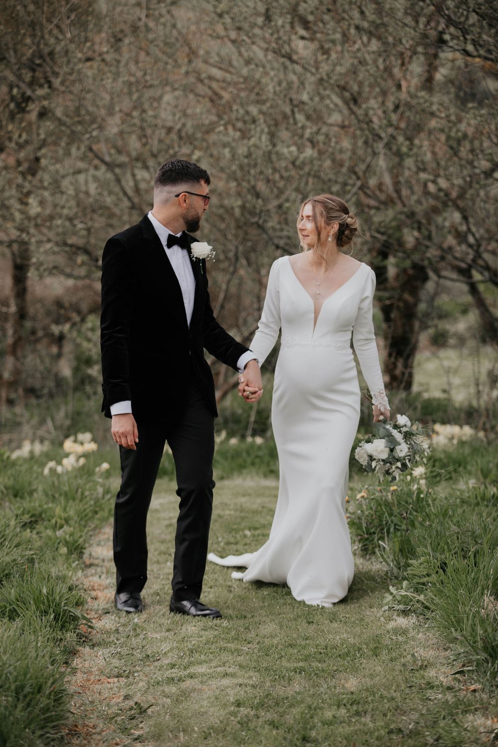 Elegant bride and groom strolling through a green woodland garden on their wedding day.