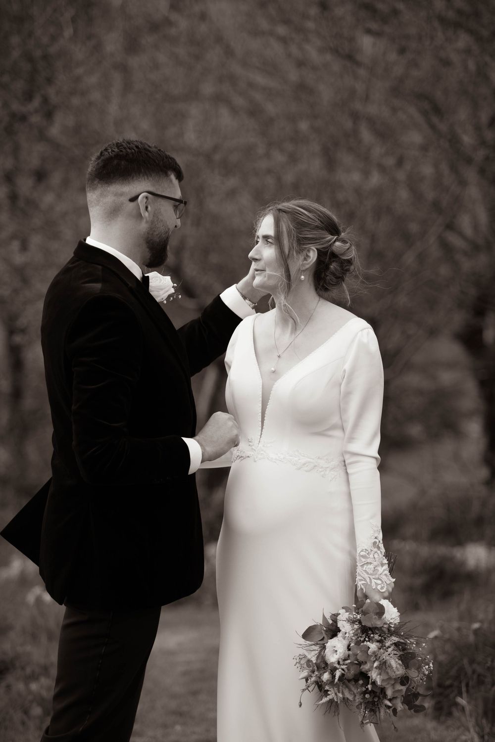 Black and white romantic portrait of groom tenderly touching bride's face outdoors.