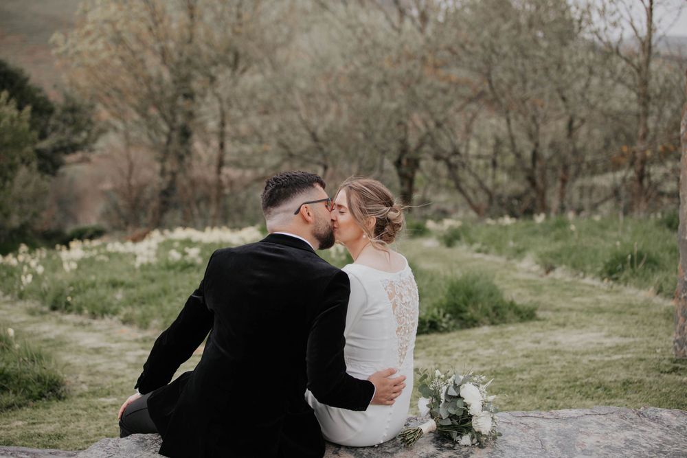 Bride and groom sharing a kiss while seated outdoors in a lush green garden setting.