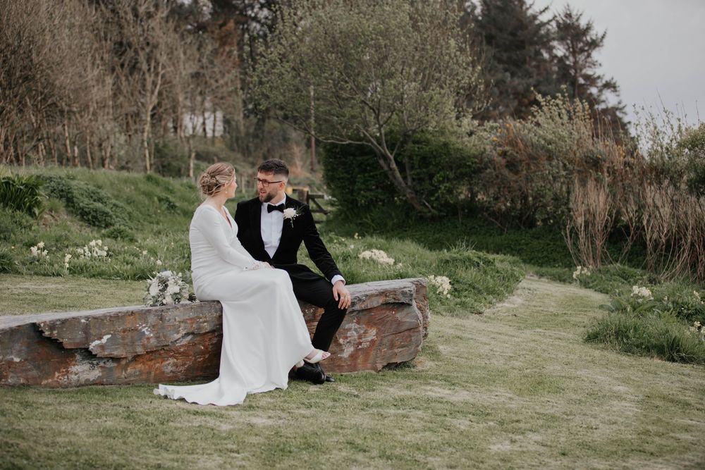 Bride and groom sitting together on a rustic wooden bench in a peaceful garden.