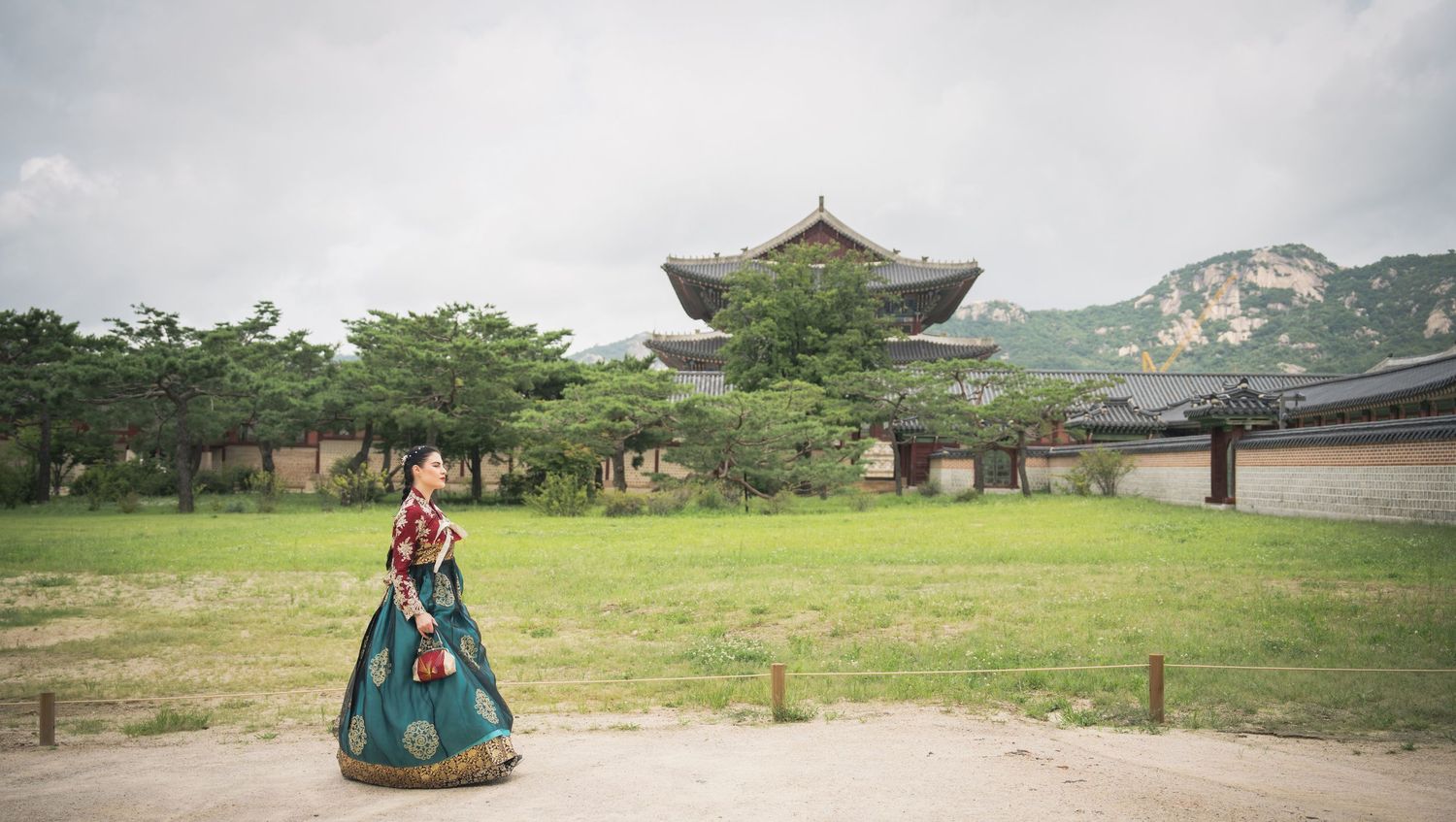 Tourists explore traditional Korean temple grounds with ornate architecture and pagodas on a cloudy summer day.