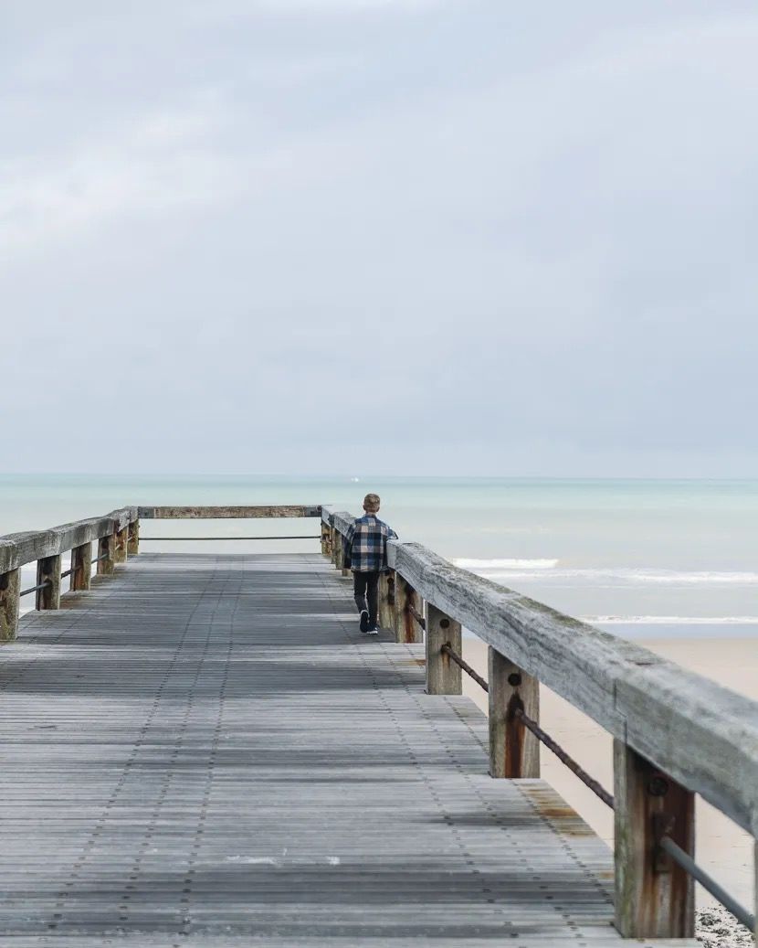 Wooden pier stretching out toward the calm sea under a soft grey sky.