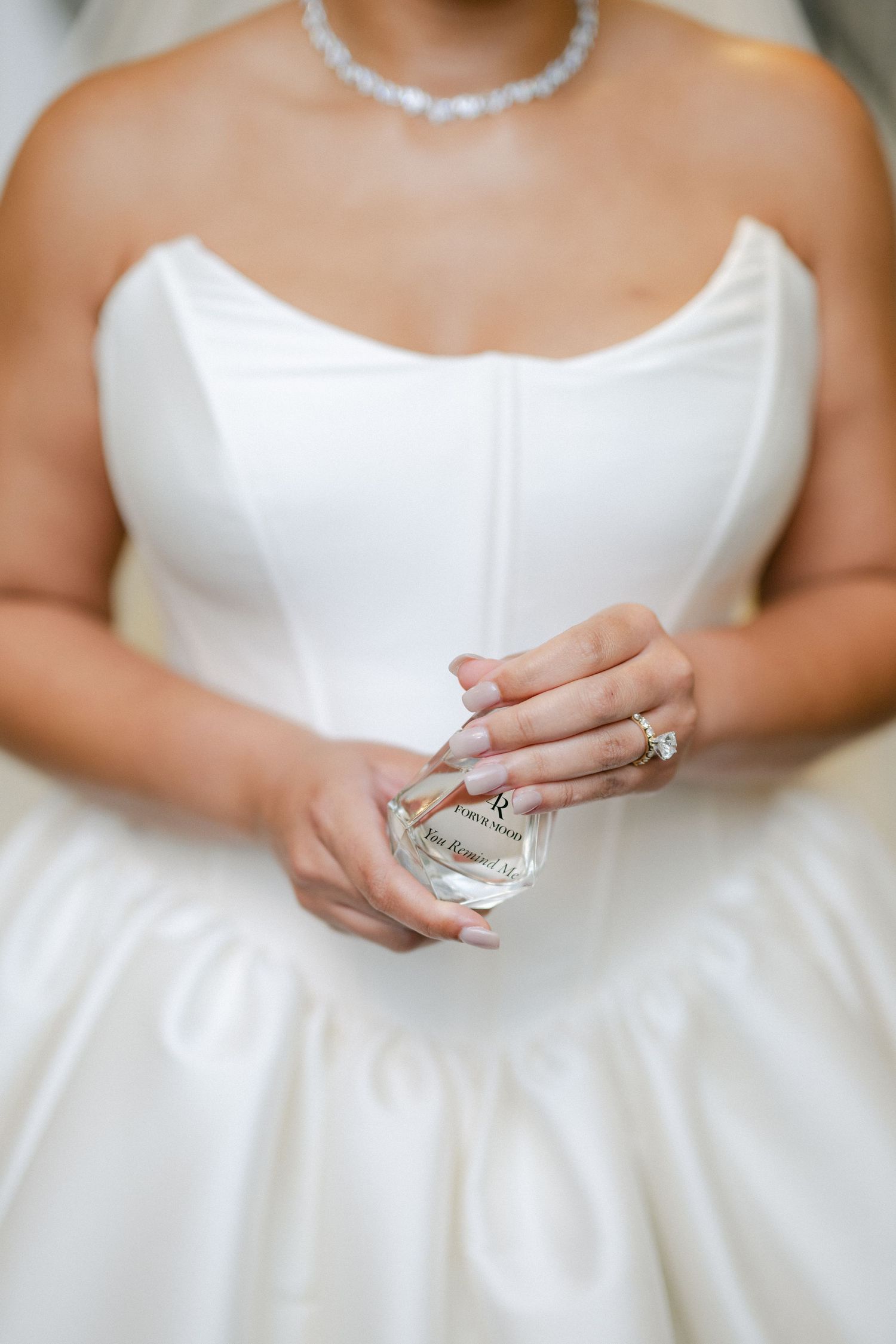 A bride in a classic white ballgown and her companion in a light blue off-shoulder dress share a joyful moment while getting ready.