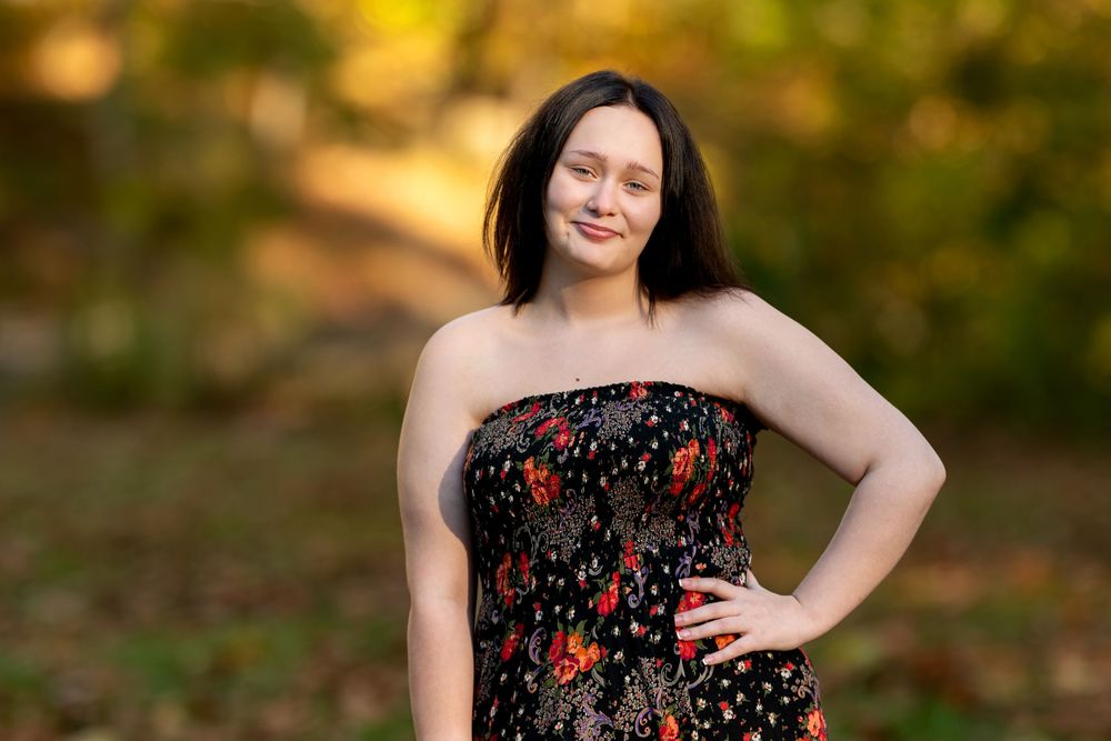 Young woman in black floral strapless dress with hand on hip in autumn park.