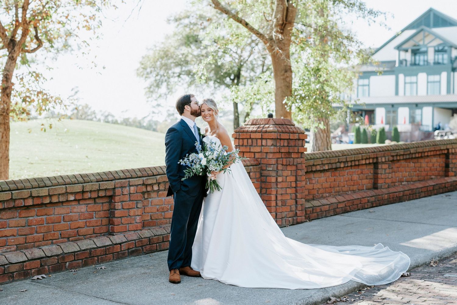 A romantic moment captured between a couple in formal wedding attire on a brick pathway during autumn.