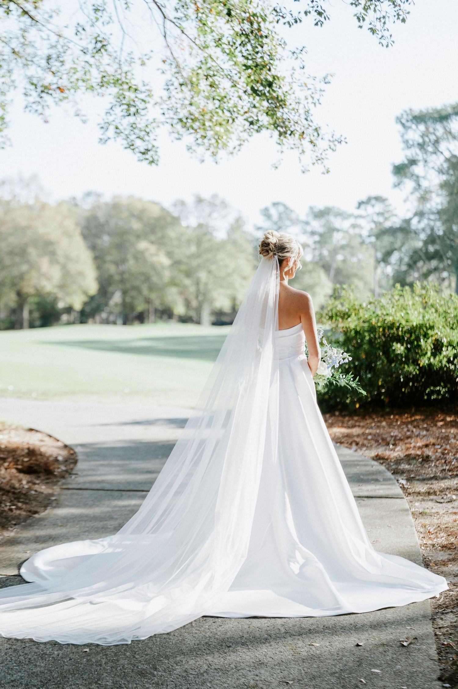 A flowing white wedding dress with a dramatic cathedral-length train creates an elegant silhouette on a winding path.