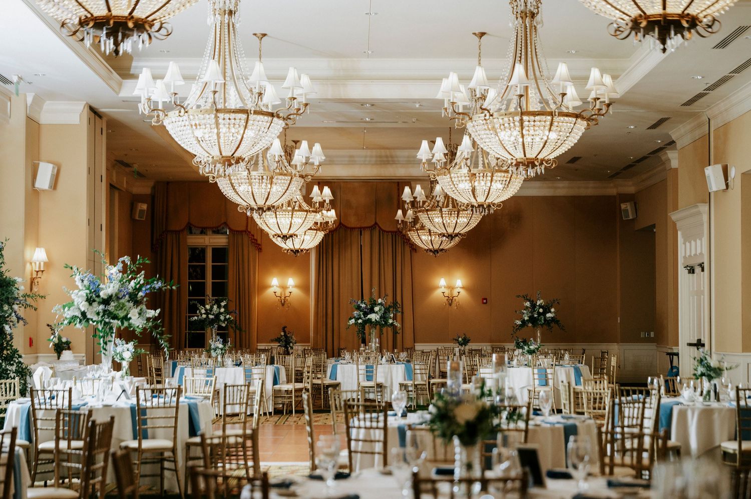 Elegant ballroom with crystal chandeliers and round tables set for a formal wedding reception.