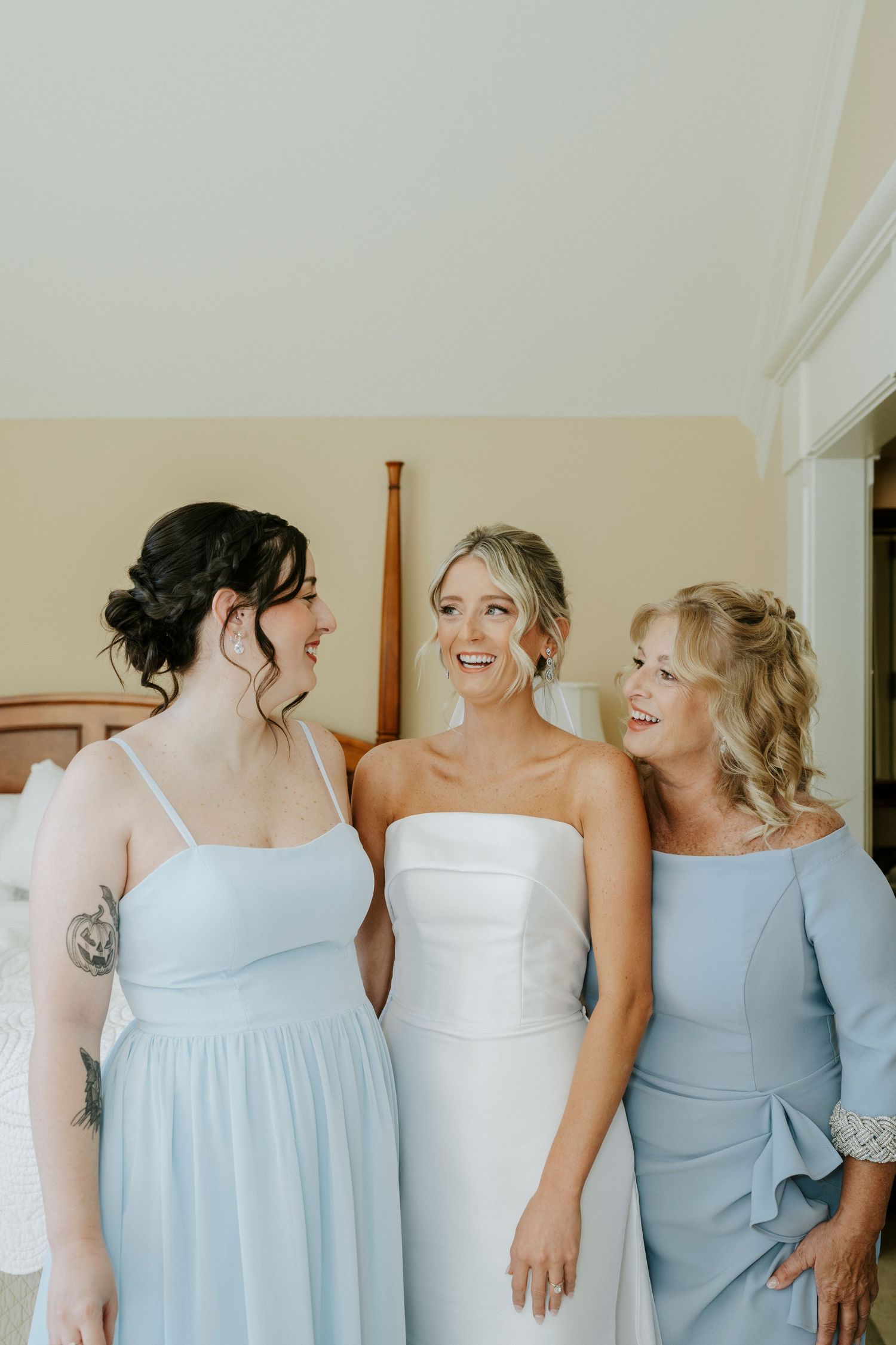 Bridesmaids in light blue dresses share a candid laughing moment during wedding preparations.