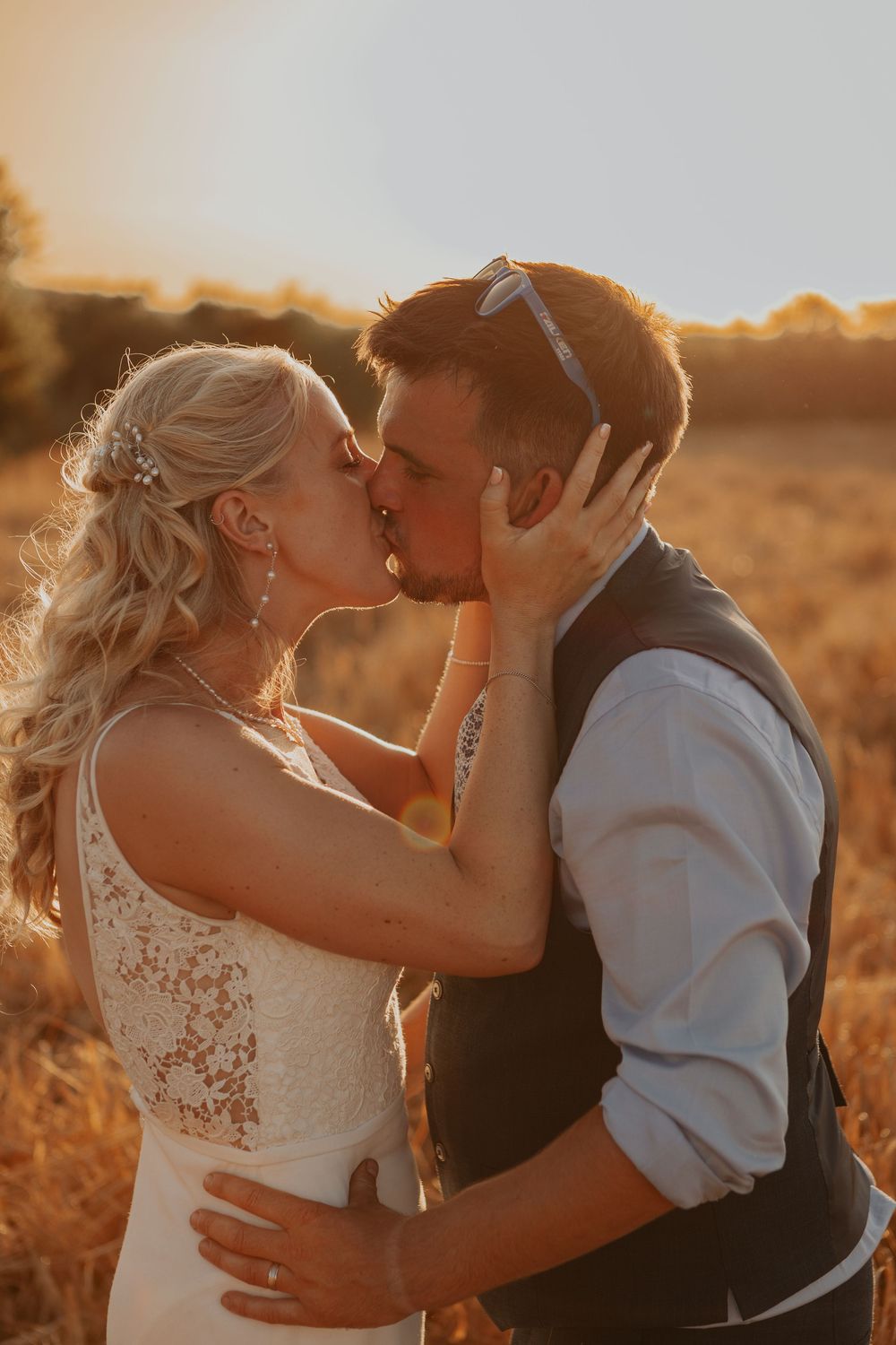 Bride and groom sharing a passionate kiss in a golden wheat field during a stunning warm sunset.