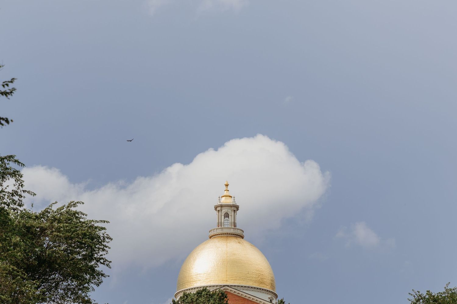 The golden dome of the Massachusetts State House rises majestically against a blue sky dotted with white clouds.