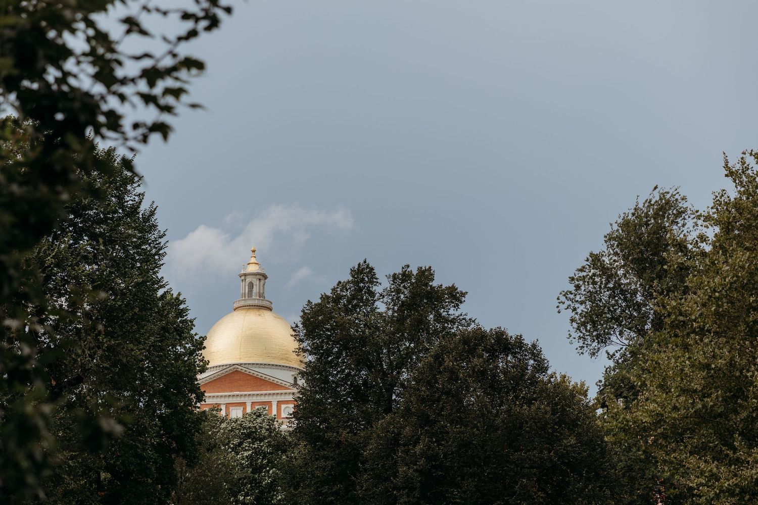 A scenic view of the Massachusetts State House golden dome peeking through autumn trees in Boston.