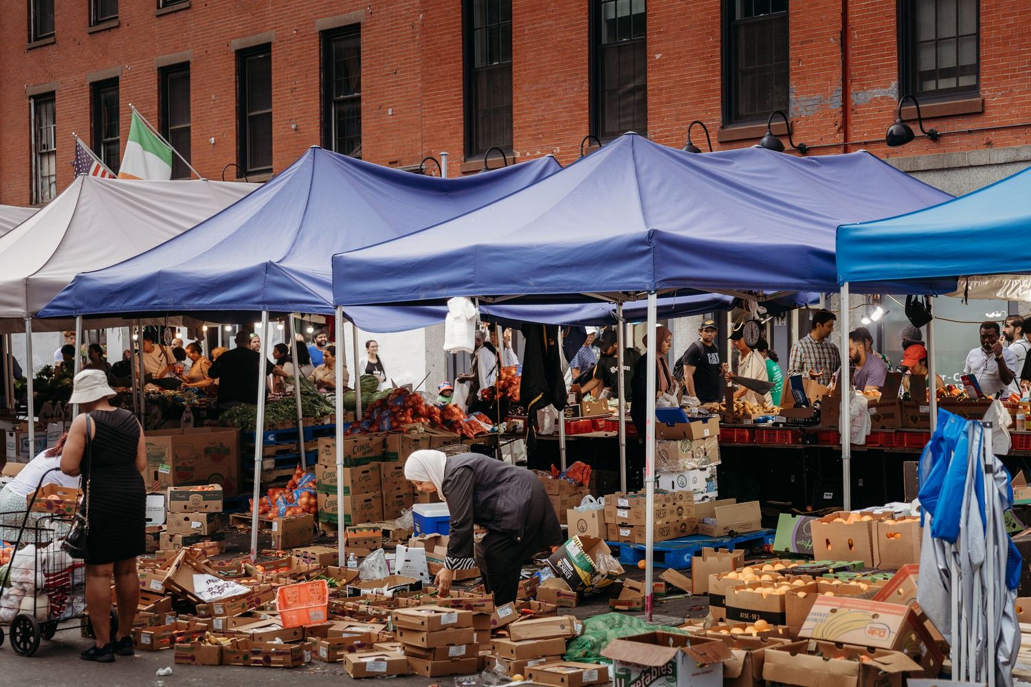 Outdoor flea market with white tents and tables displaying antiques and vintage items along a brick building.