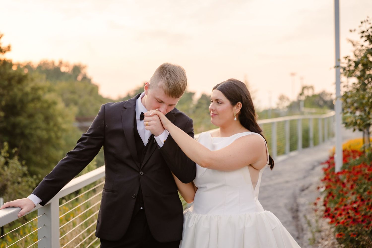 A romantic couple in wedding attire share joyful moments together in an outdoor garden setting at sunset.