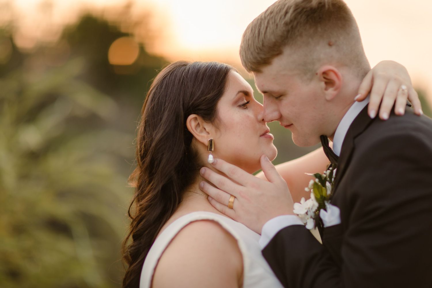 Romantic wedding couple embraces at sunset with golden light creating a warm, intimate atmosphere.
