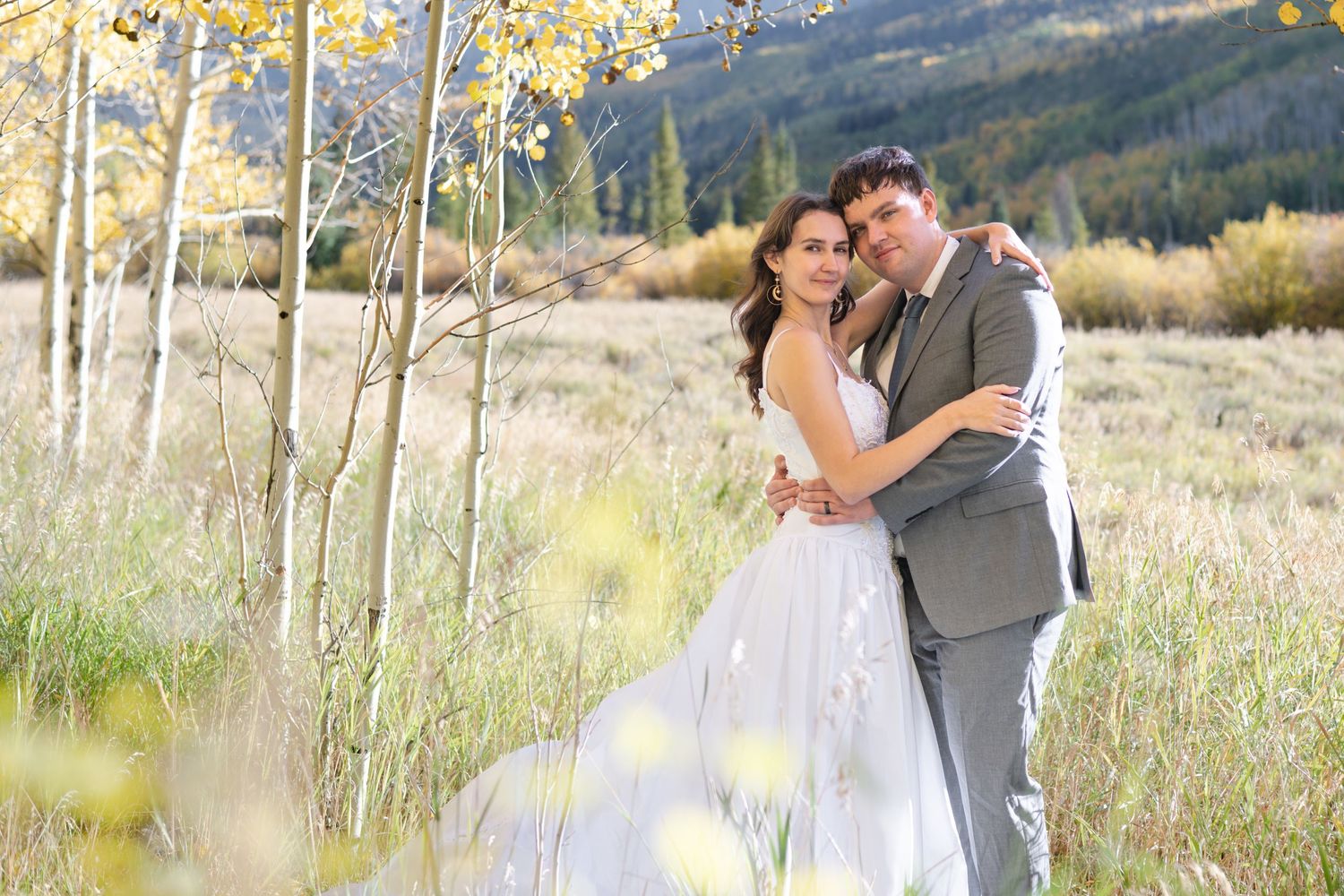 A ride and groom embracing in a golden meadow with aspen trees during an outdoor fall elopement wedding.