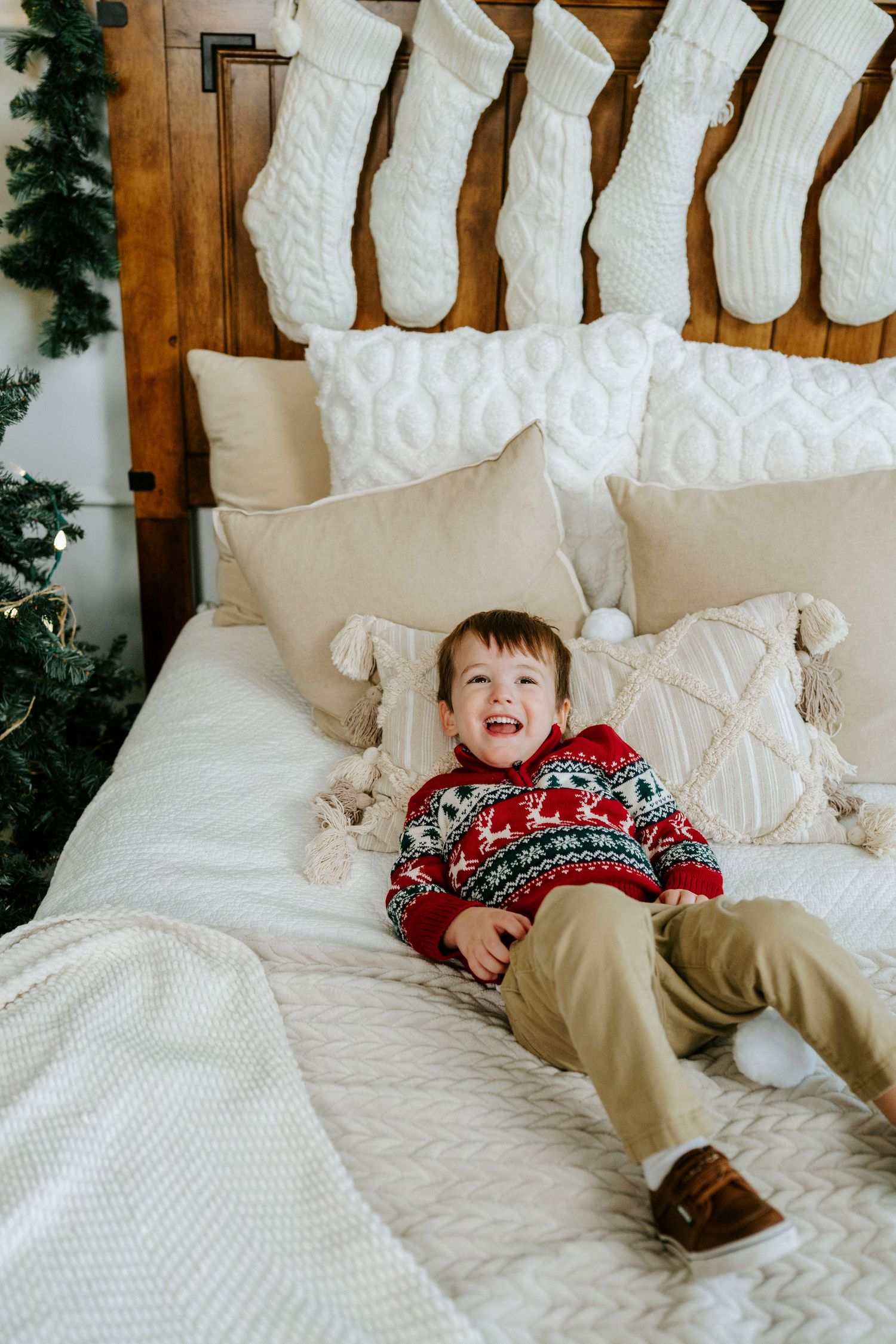 White Christmas stockings hang on wooden wall above cozy bed with festive holiday decor.