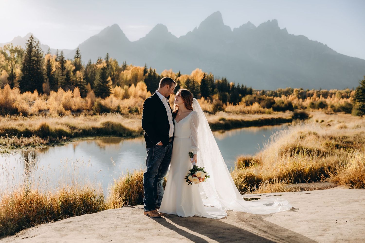 Wedding couple embraces against dramatic mountain backdrop at sunset in Grand Teton National Park.