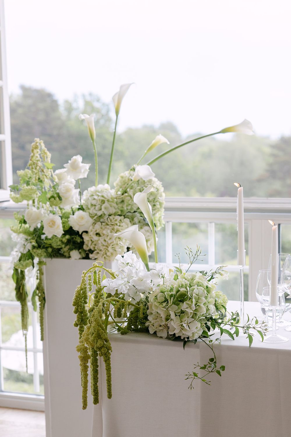 Bon Viola, Elegant white floral arrangements with hydrangeas and lilies displayed along a window ledge in a modern event space. Bröllopsfoto