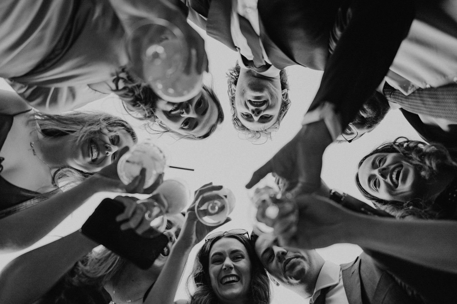 Black and white circular composition of wedding party looking down at camera with playful expressions.