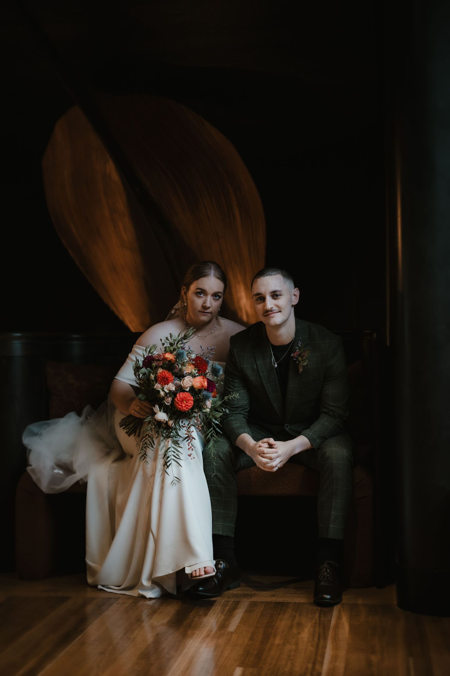 A moody wedding portrait of a couple with dramatic lighting and a colorful bouquet.