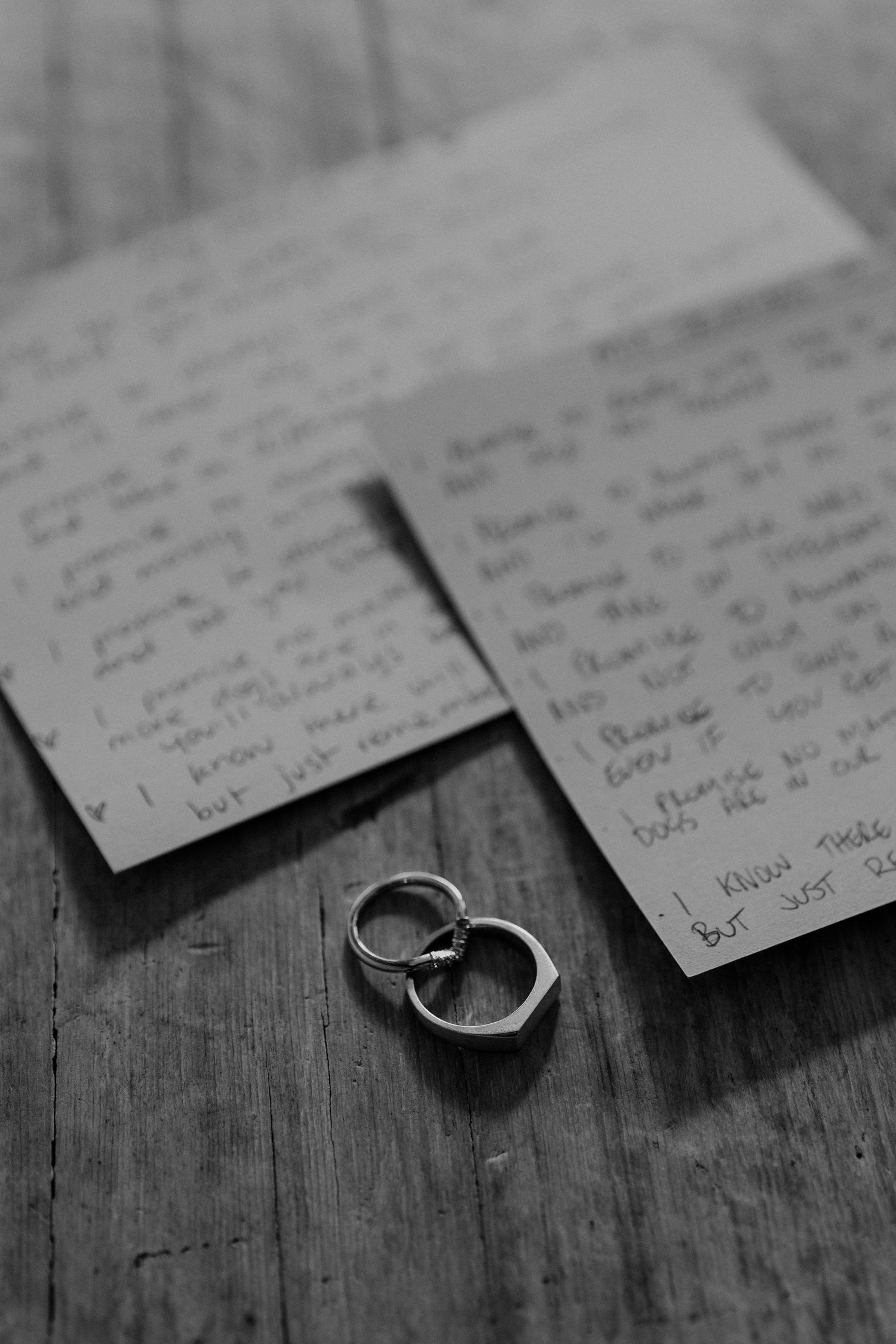 A wedding ring rests on a dark wooden surface beside handwritten notes in black and white.