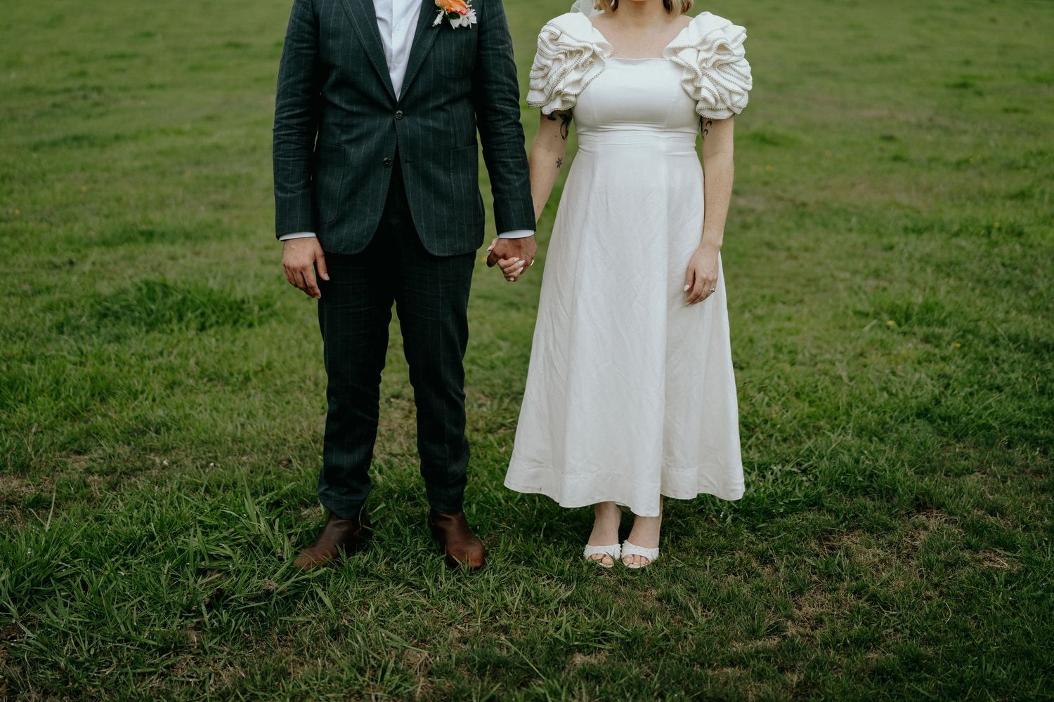 A couple in wedding attire stands together on a lush green lawn during their outdoor ceremony.