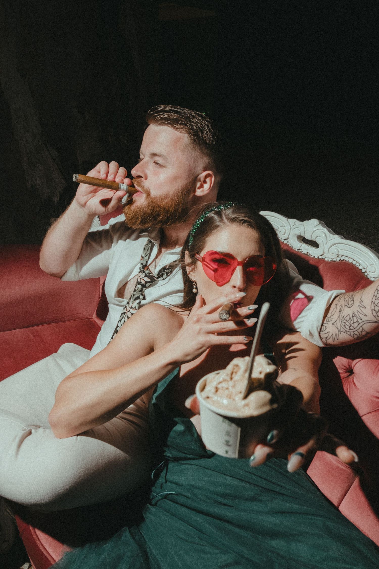 Wedding guests relaxing on red velvet couch during reception celebrations.