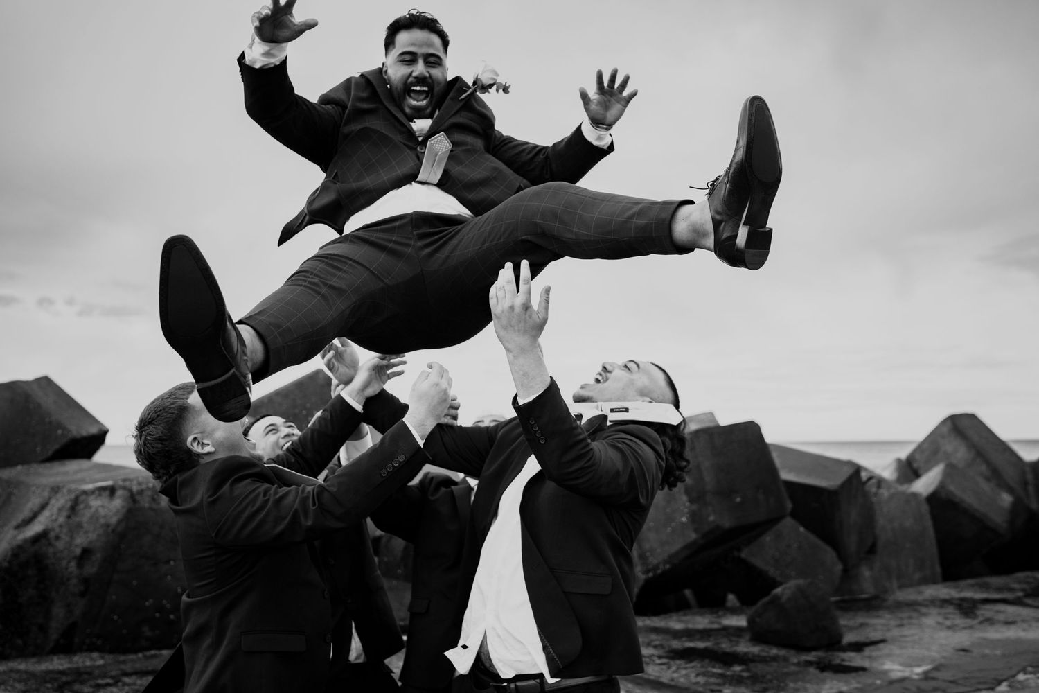 Playful black and white photos of groomsmen being lifted in air during wedding festivities.