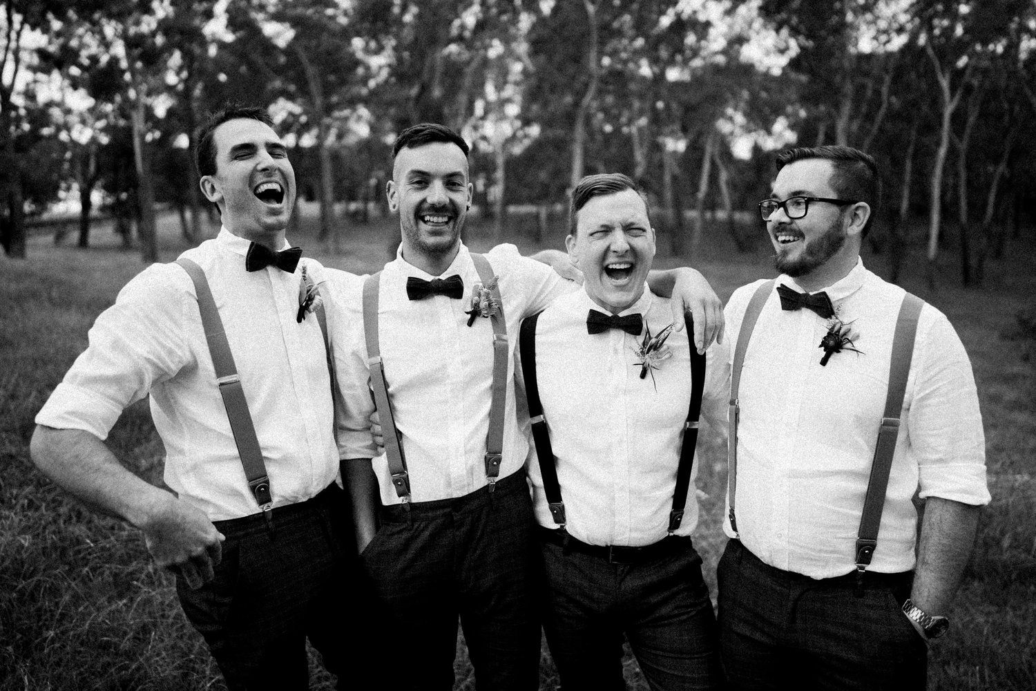 Groomsmen in white shirts and suspenders pose together for a fun group photo.
