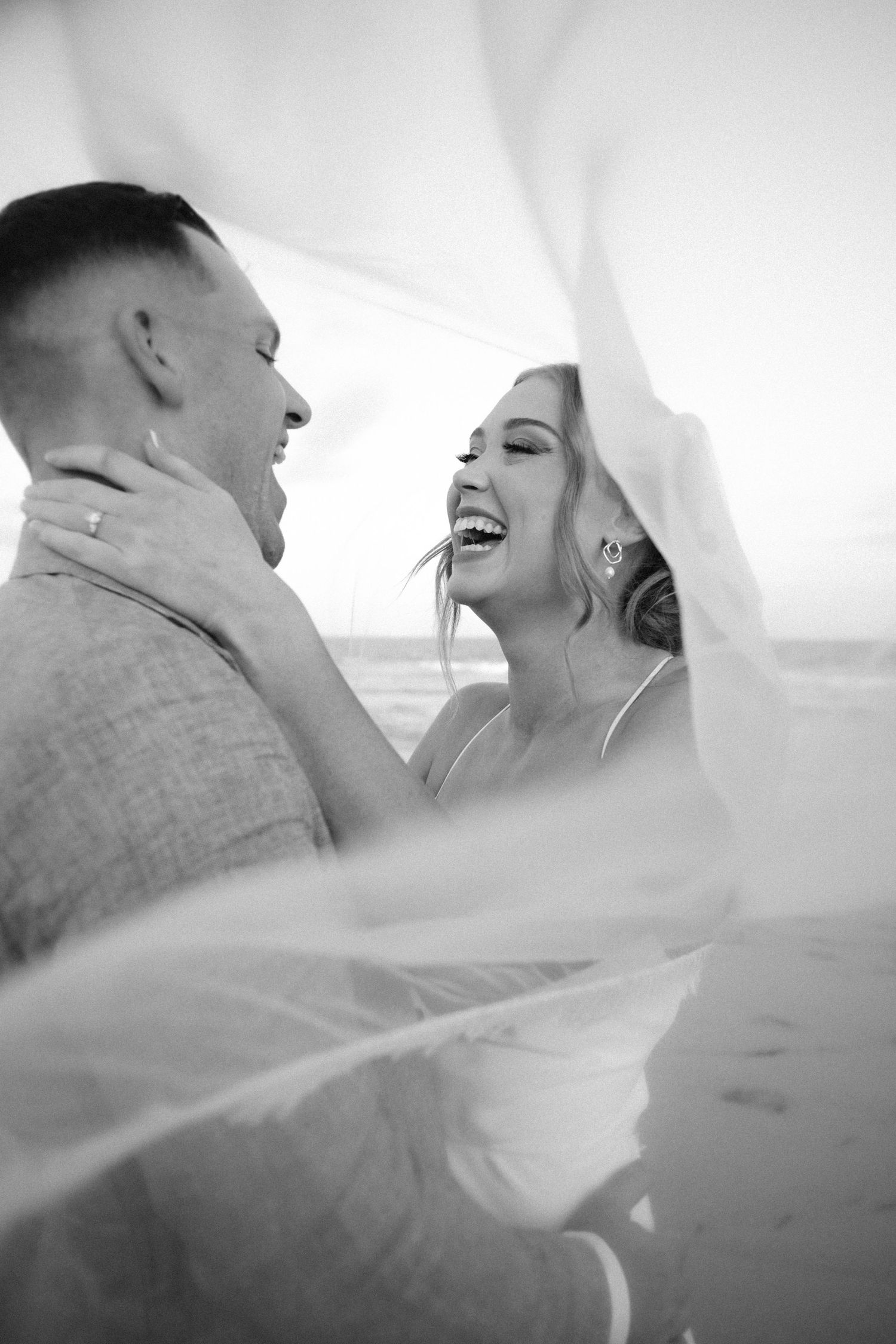 A joyful wedding moment captured through a veil as a couple shares laughter together.