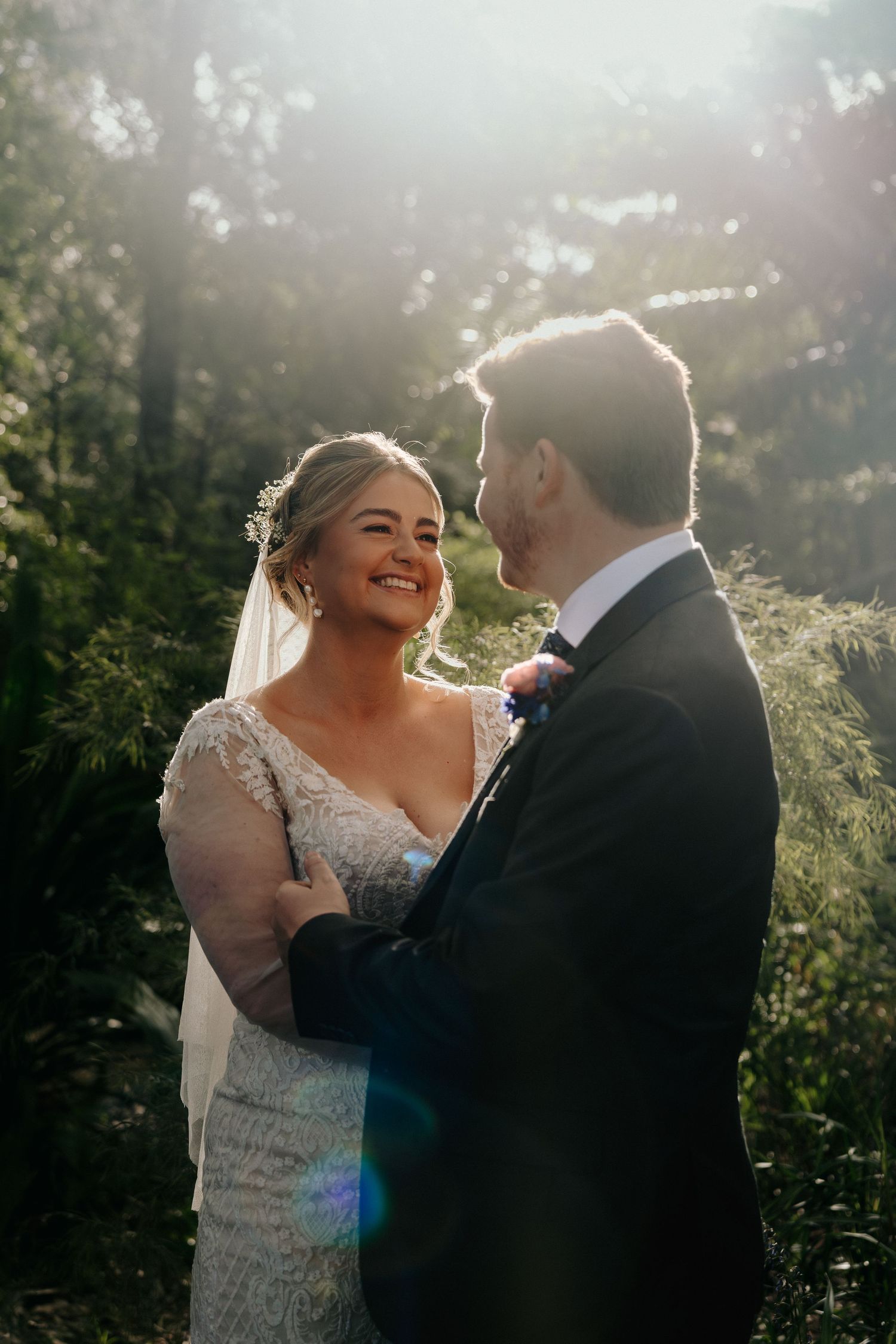 Romantic wedding couple embraces in golden sunlight with lens flares creating a dreamy outdoor atmosphere.