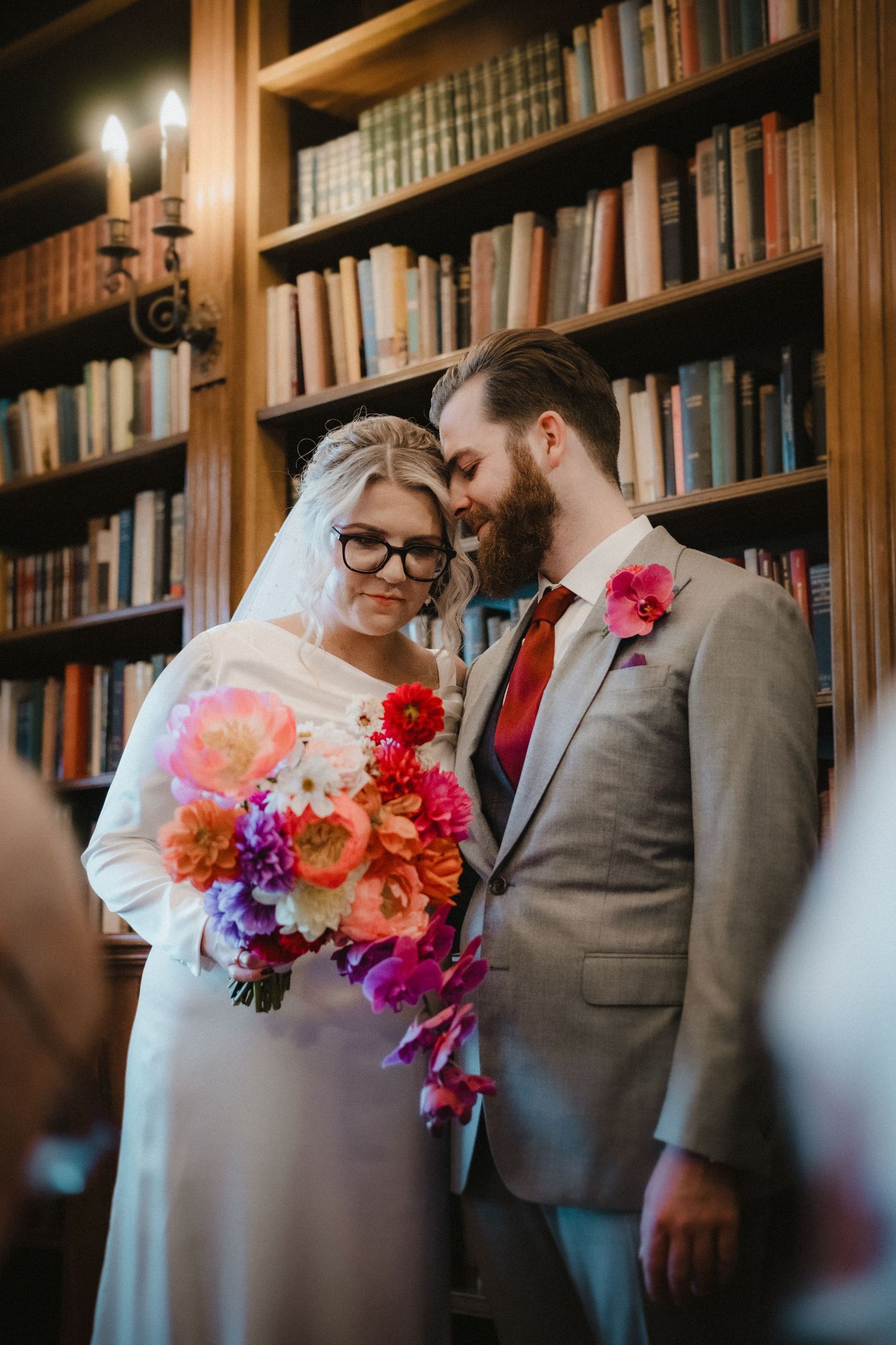 A romantic moment captured in a library setting with vibrant floral bouquets.