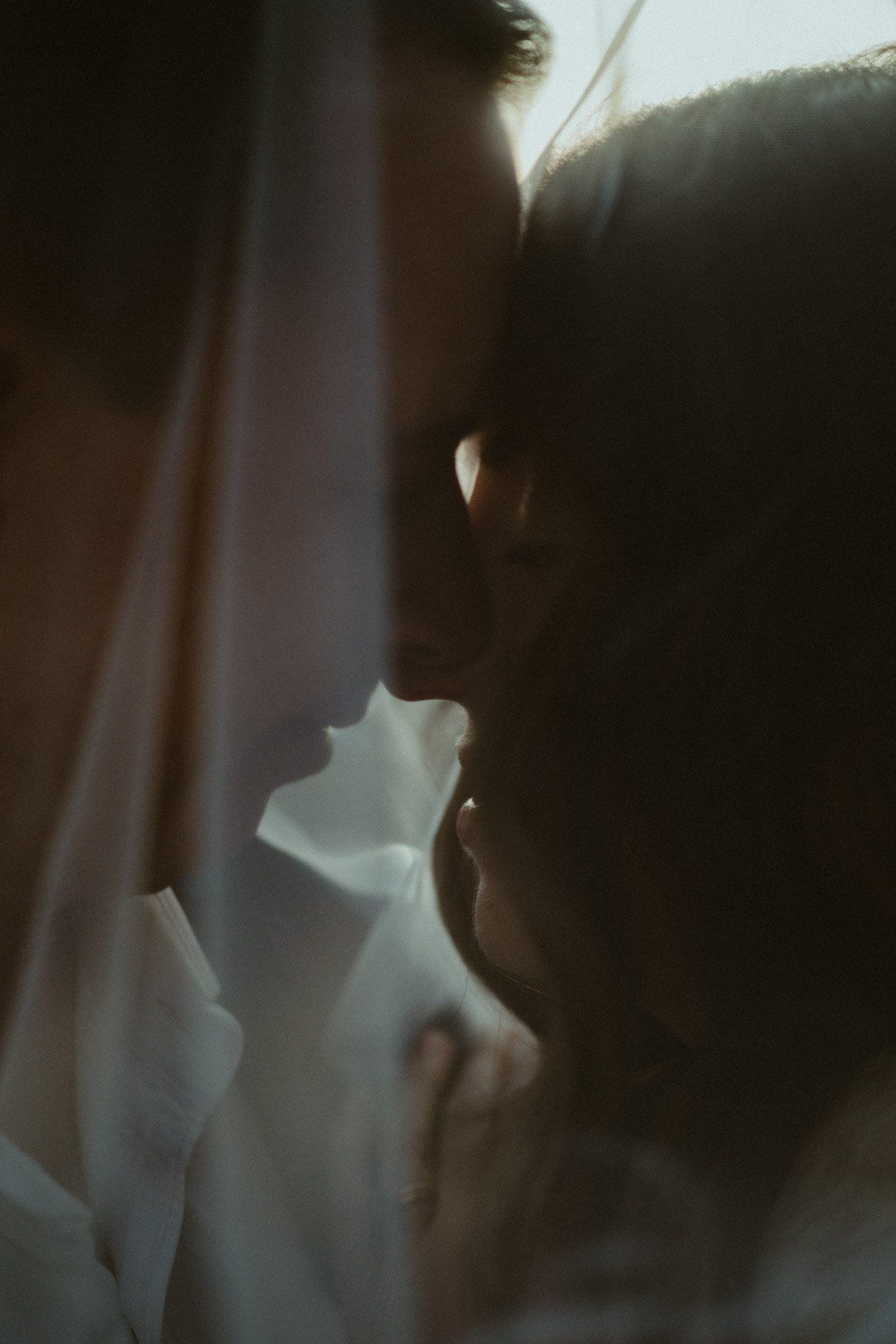 Silhouetted close-up profiles of a couple in an intimate moment against a dark background.