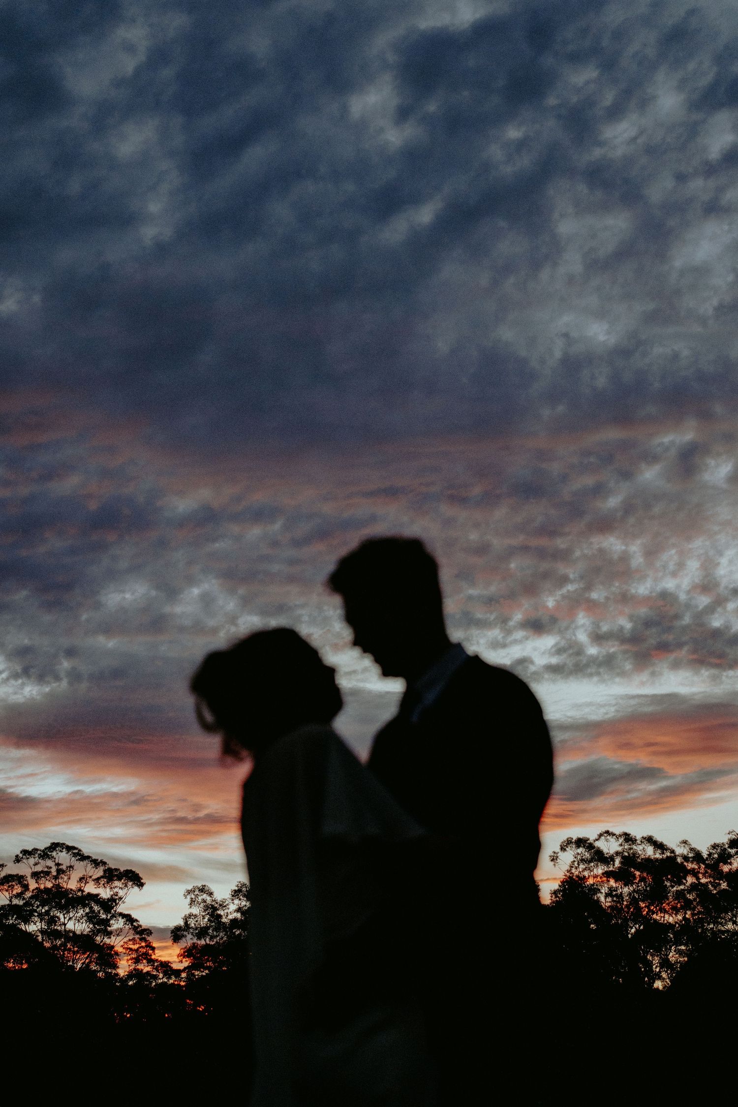 Silhouette of a couple facing each other against a dramatic sunset sky with colorful clouds at dusk.