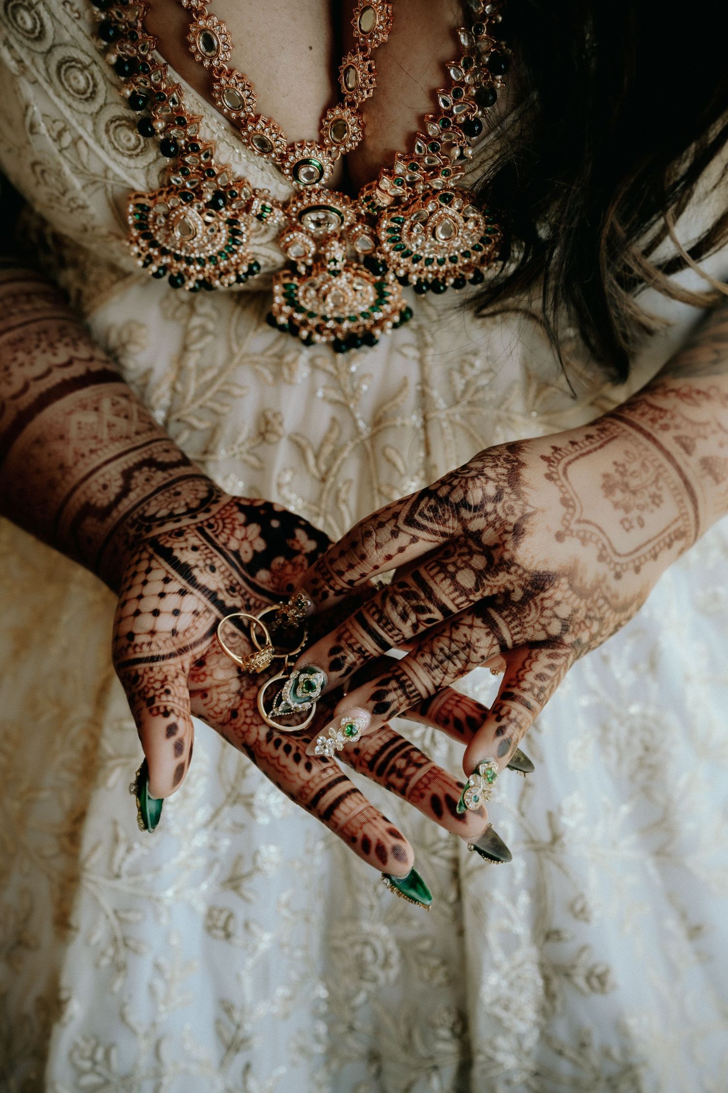 Detailed henna mehndi designs on hands resting against white lace fabric with ornate jewelry details.